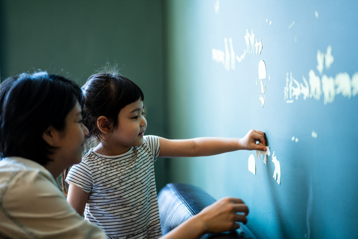 A child and adult exploring stickers together on a blue wall
